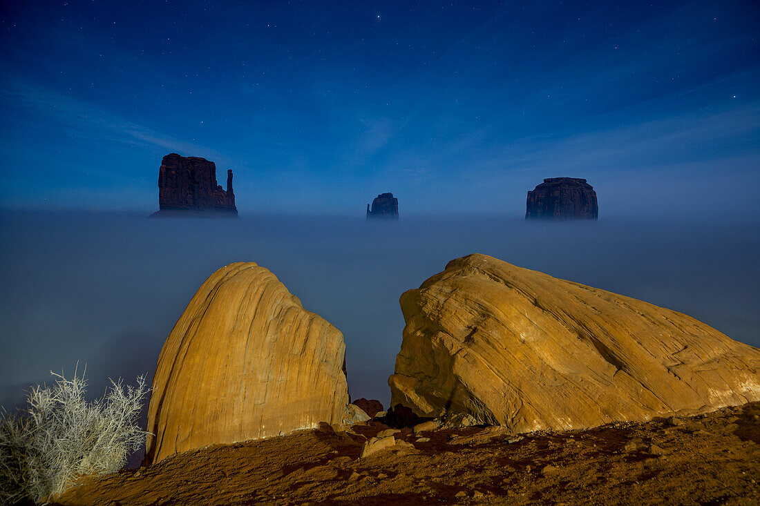 Ground fog obscures the base of the Mittens at night with stars overhead in the Monument Valley Navajo Tribal Park in Arizona.
