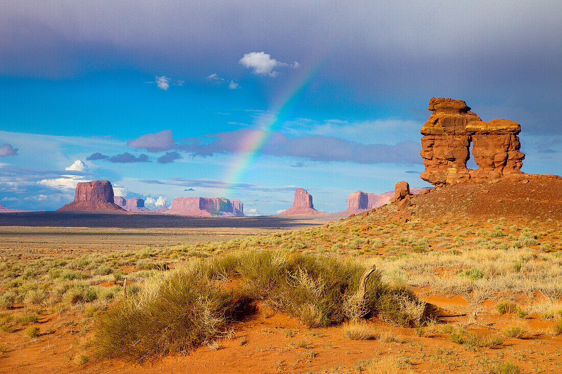 Ein Regenbogen im Mystery Valley im Monument Valley Navajo Tribal Park in Arizona. Dahinter befinden sich, von links nach rechts: Mitchell Butte, Brigham's Tomb und Grey Whiskers Butte in der Ferne