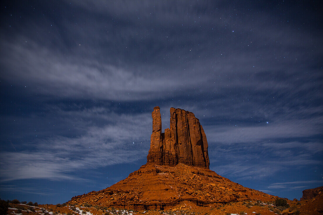 Winter stars & clouds over the moonlit West Mitten at night in the Monument Valley Navajo Tribal Park in Arizona.