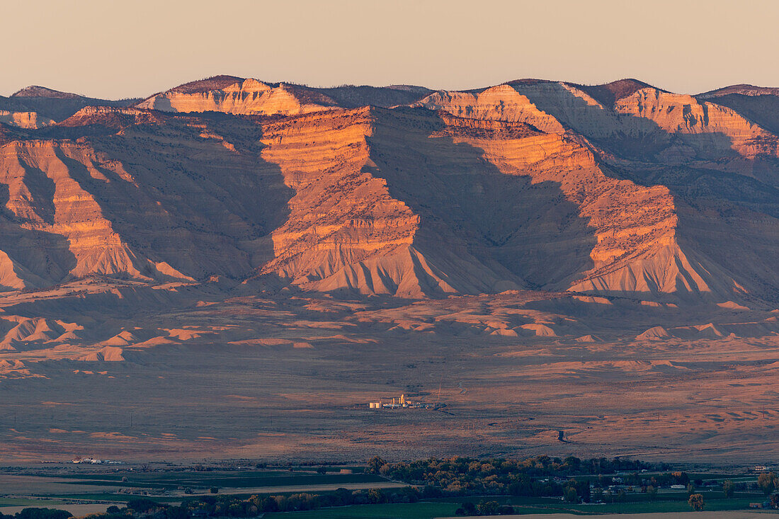 Die Book Cliffs und das Grand Valley in der Nähe von Fruita, Colorado, bei Sonnenuntergang. In der Mitte befindet sich eine kleine Erdölraffinerie
