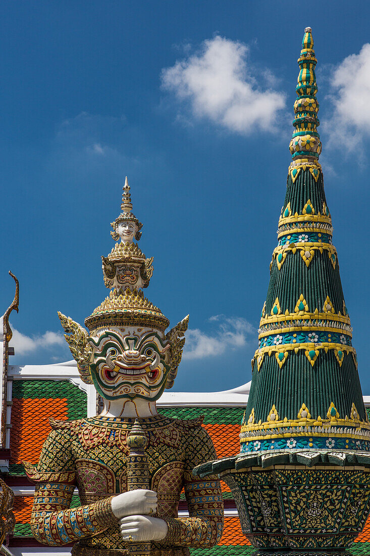 A yaksha guardian statue at the Temple of the Emerald Buddha complex in the Grand Palace grounds in Bangkok, Thailand. At right is a Panom Mak sculpture. A yaksha or yak is a giant guardian spirit in Thai lore.