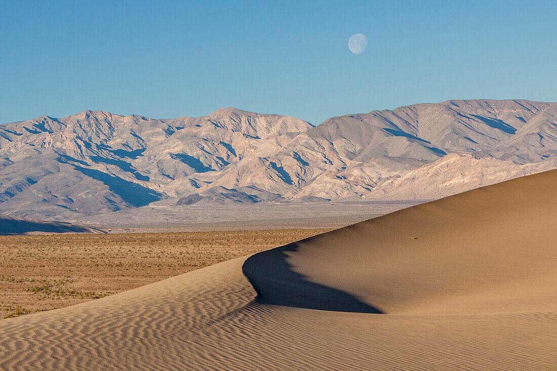 Setting moon over the Mesquite Flat sand dunes & Panamint Mountains in Death Valley National Park in the Mojave Desert, California.