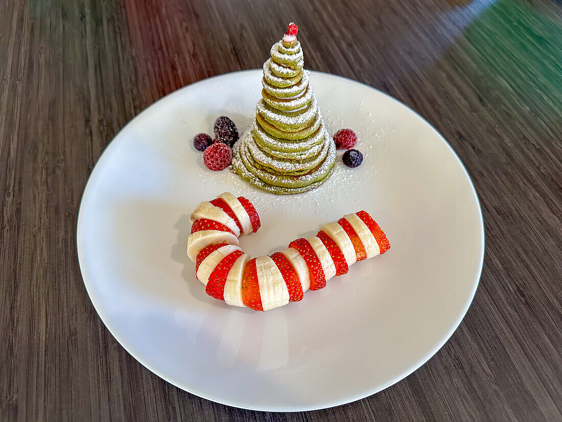A Christmas holiday breakfast with a pancake Christmas tree and a banana & strawberry candy cane.