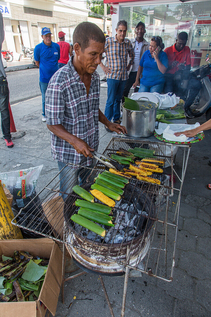 Ein Mann kocht dominikanische Tamales über einem offenen Grill auf der Straße bei der Bani Mango Expo in Bani, Dominikanische Republik