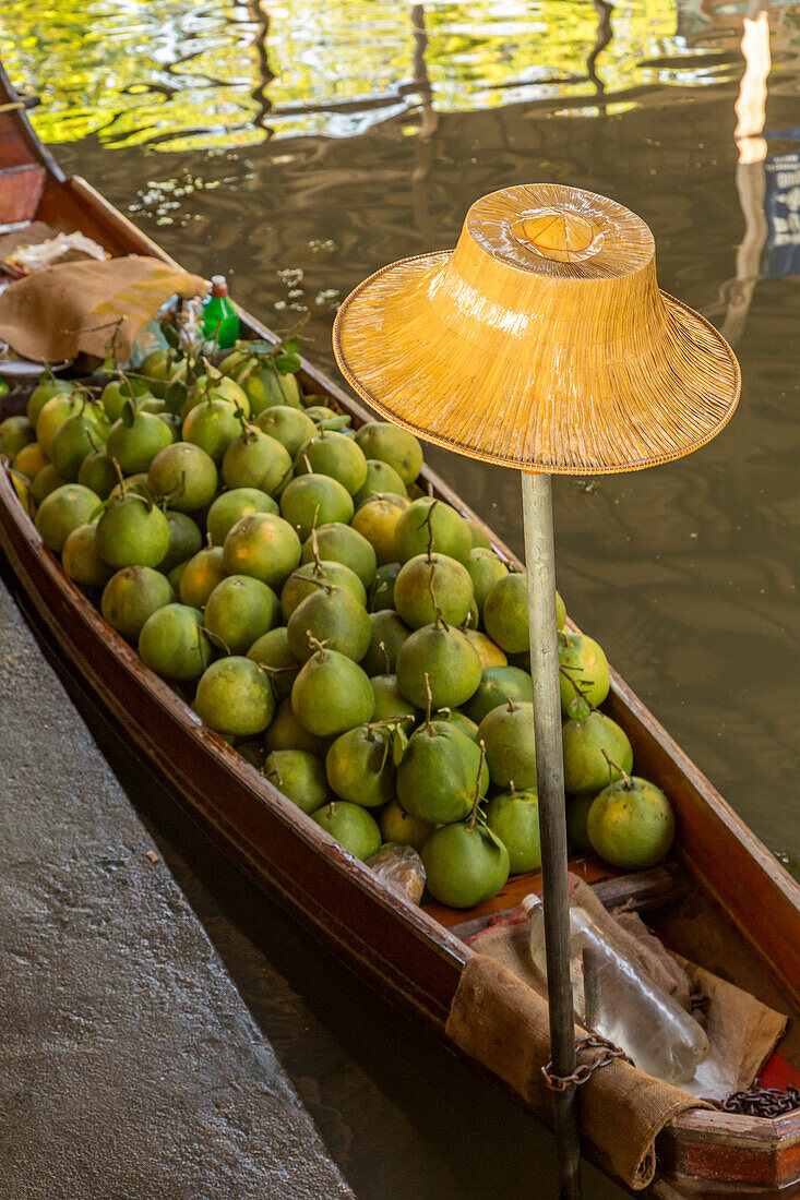 Ein traditioneller thailändischer Hut und Sapodilla-Früchte, die auf einem Boot auf dem schwimmenden Markt von Damnoen Saduak in Thailand verkauft werden