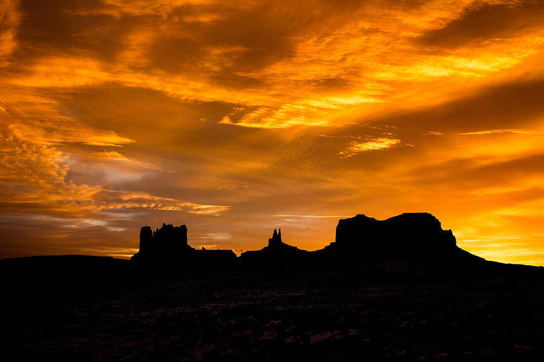 Colorful sunset skies over the Utah monuments in the Monument Valley Navajo Tribal Park in Utah & Arizona. L-R: Castle Butte & the Stagecoach, King on the Throne & Brigham's Tomb.