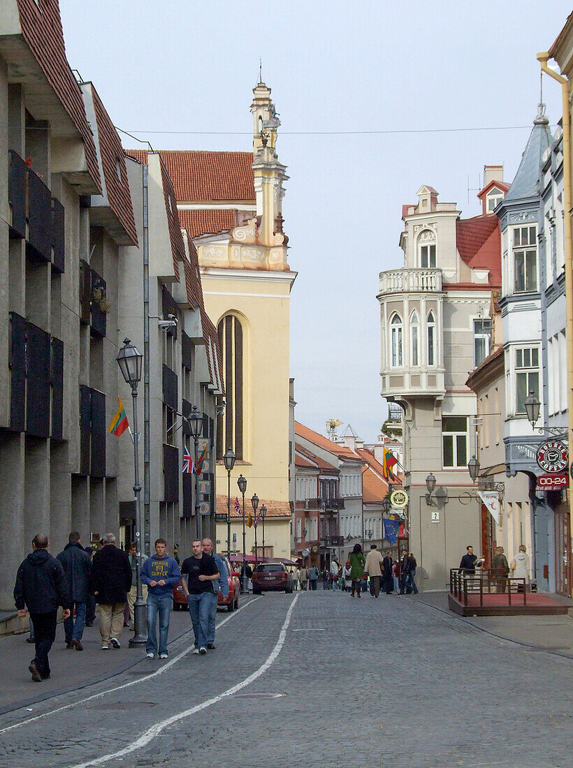 People walk on a street of classic architecture in the historic Old Town of Vilnius, Lithuania. The Church of St. Johns is at left. A UNESCO World Heritage Site.