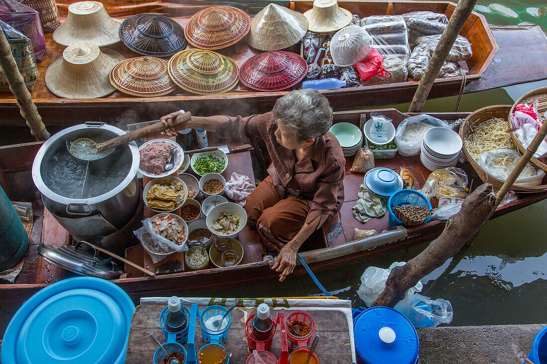 Eine thailändische Frau bei der Zubereitung von Speisen auf ihrem schwimmenden Küchenboot auf dem Damnoen Saduak Floating Market in Thailand