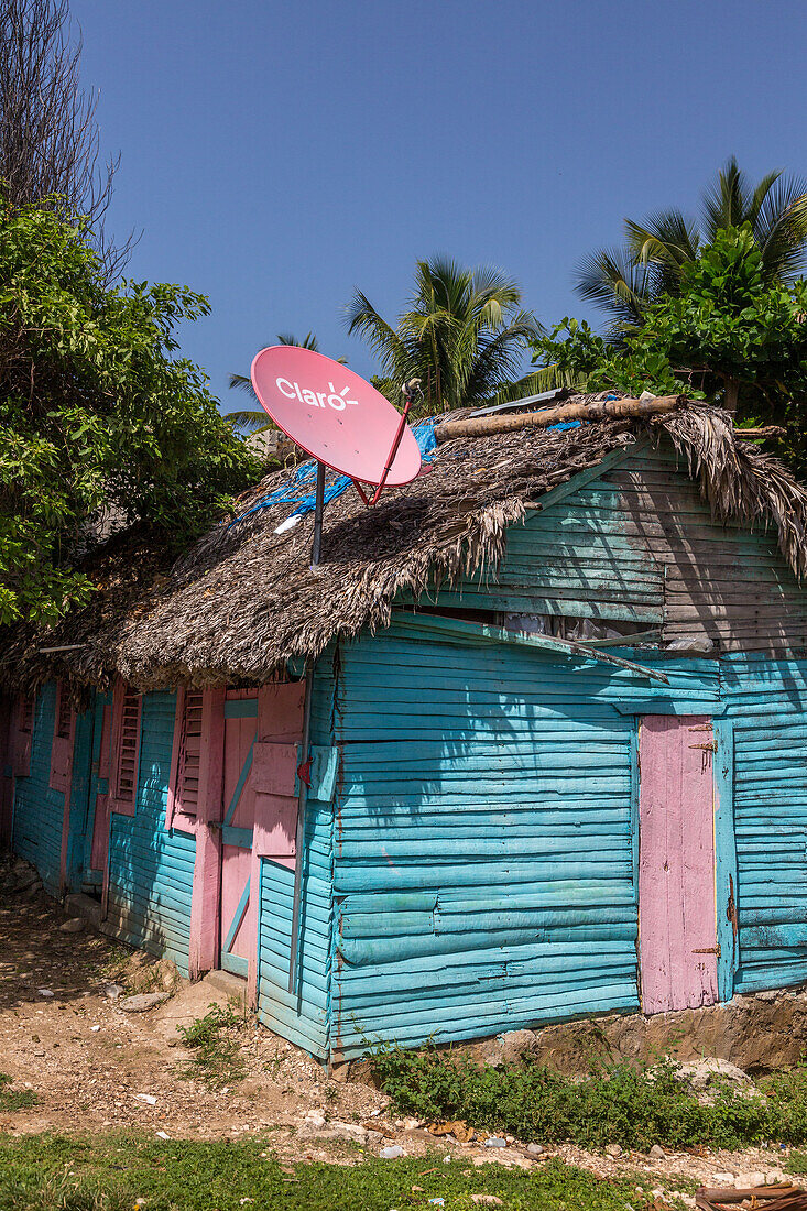 Ein kleines, traditionelles Holzhaus mit Strohdach und Satellitenschüssel in der ländlichen Dominikanischen Republik
