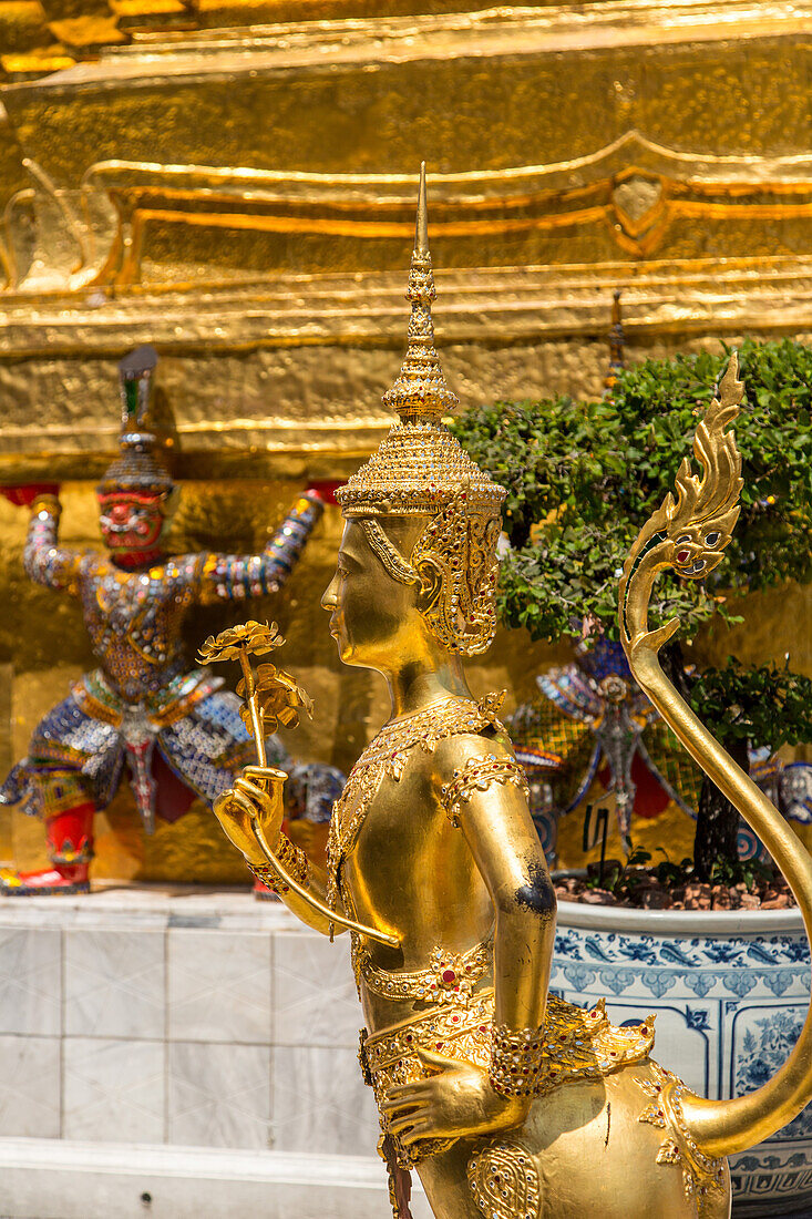 Golden statue of a mythical Thepnorasi guards the Temple of the Emerald Buddha in the Grand Palace complex in Bangkok, Thailand.