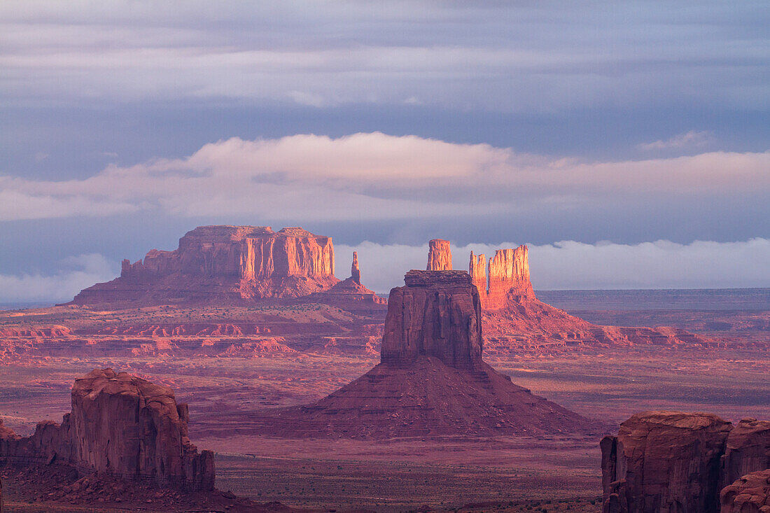 Sonnenaufgang im Monument Valley Navajo Tribal Park in Arizona mit dem East Mitten in der Mitte und den Monumenten von Utah dahinter. Brigham's Tomb links, Bear & Rabbit und die Postkutsche rechts