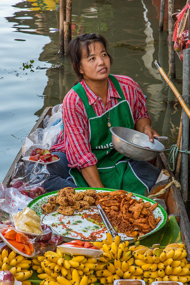 Eine thailändische Frau bereitet auf ihrem Boot auf dem schwimmenden Markt von Damnoen Saduak in Thailand Essen zu
