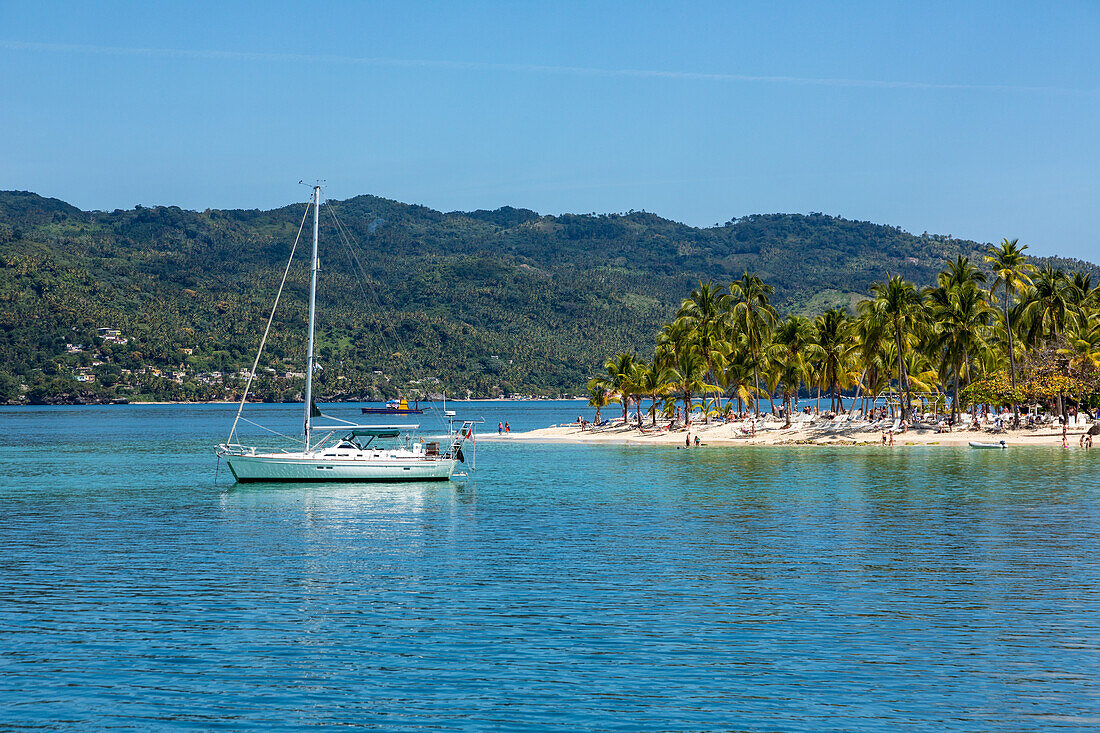 Ein Segelboot und Touristen am Strand von Cayo Levantado, einer Ferieninsel in der Bucht von Samana in der Dominikanischen Republik