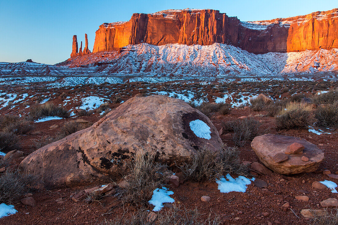 A lichen-covered boulder in front of the Three Sisters and Mitchell Mesa in the Monument Valley Navajo Tribal Park in Arizona.