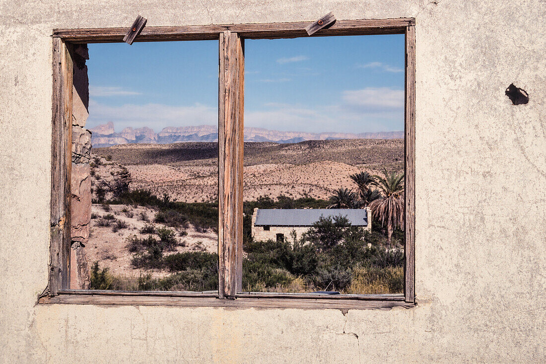 Das Fenster einer alten Ruine in Hot Springs umrahmt die Wüstenlandschaft und das alte Postamt im Big Bend National Park in Texas. In der Ferne sind die Berge der Sierra del Carmen in Mexiko zu sehen.