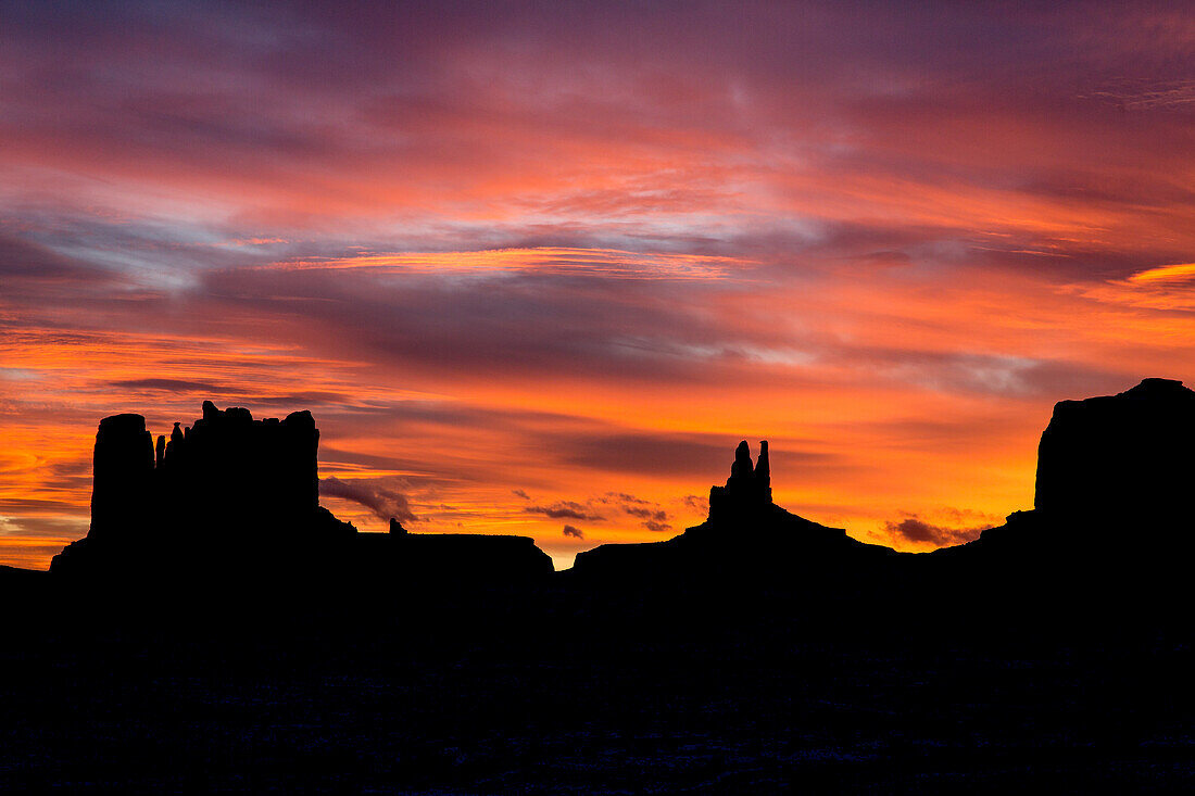 Farbenfroher Sonnenuntergang über den Monumenten von Utah im Monument Valley Navajo Tribal Park in Utah und Arizona. L-R: Castle Butte & die Postkutsche, König auf dem Thron & Brigham's Tomb