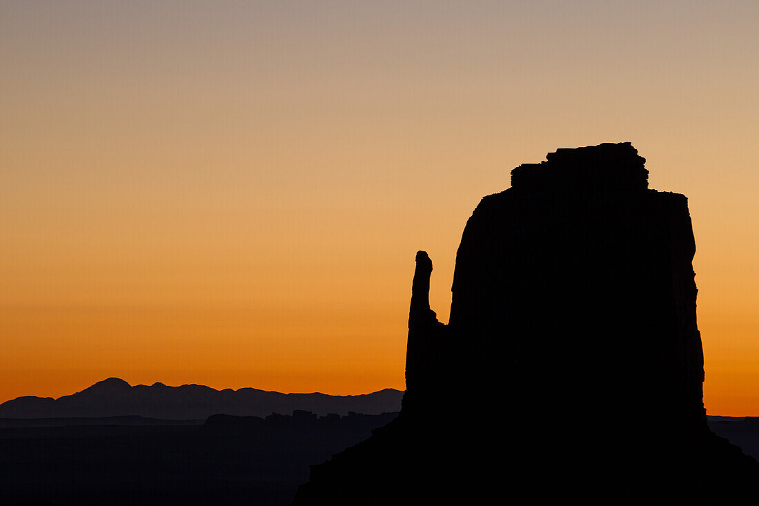 Pastel sunrise sky behind the East Mitten Butte in the Monument Valley Navajo Tribal Park in Arizona.