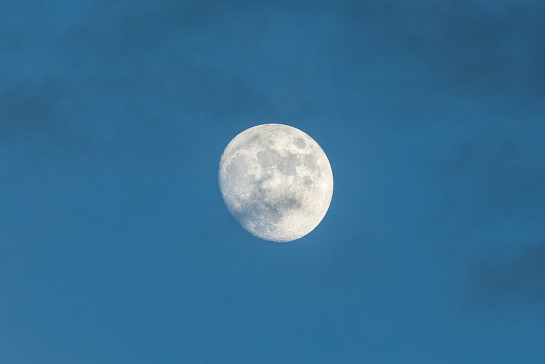 A waxing gibbous moon with clouds photographed in the daytime with a telephoto lens over New Mexico.