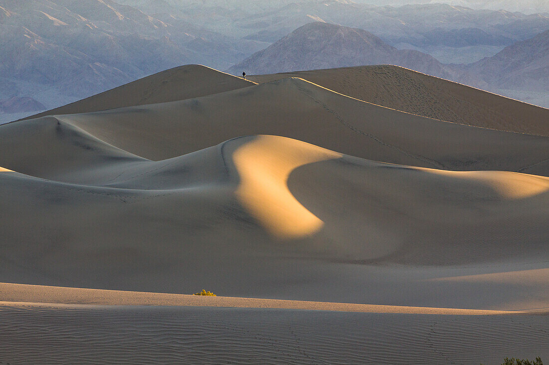 Sunrise on the Mesquite Flat sand dunes in Death Valley National Park in the Mojave Desert, California. A photographer climbs a dune.