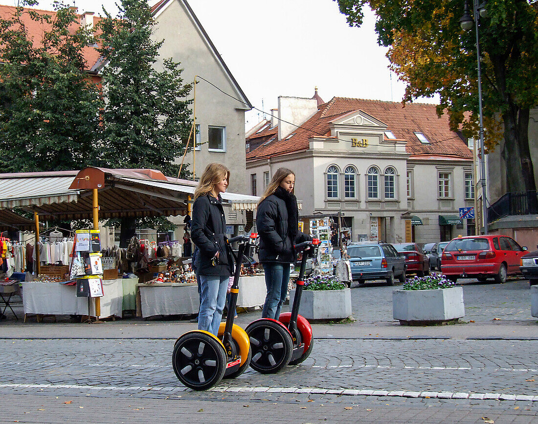 Two girls ride Segways on the street in the medieval Old Town of Vilnius, Lithuania. A UNESCO World Heritage Site.
