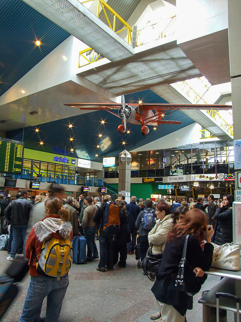 Passagiere im älteren Terminal des Internationalen Flughafens Vilnius in Litauen. Eine Reproduktion der "Lituanica" hängt von der Decke