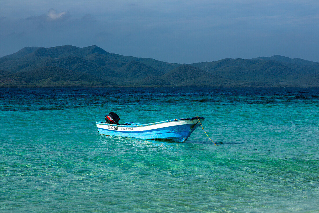 Ein Motorboot liegt im klaren, flachen Wasser um Cayo Arena oder Paradise Island vor Anker. Im Hintergrund ist der Nationalpark Monte Cristi in der Dominikanischen Republik, Hispaniola, zu sehen.