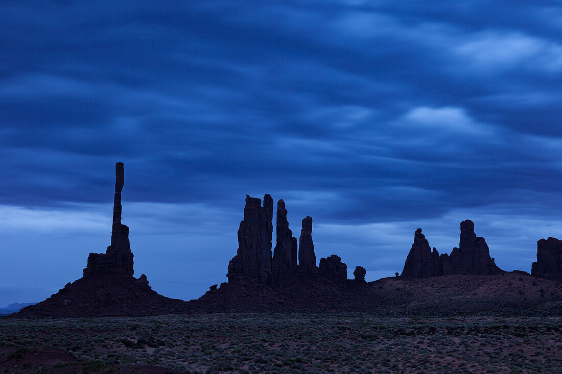 The Totem Pole and the Yei Bi Chei with clouds before dawn in the Monument Valley Navajo Tribal Park in Arizona.