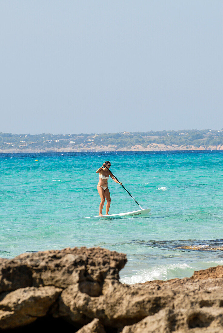 Junge Frau beim Paddelsurfen am Strand von Migjorn, Formentera