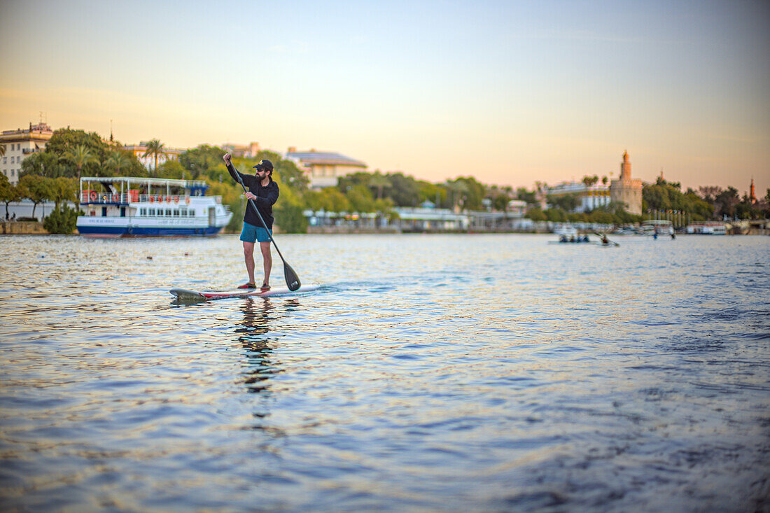 Mann übt Paddelsurfen auf dem Fluss Guadalquivir im Zentrum von Sevilla, Spanien