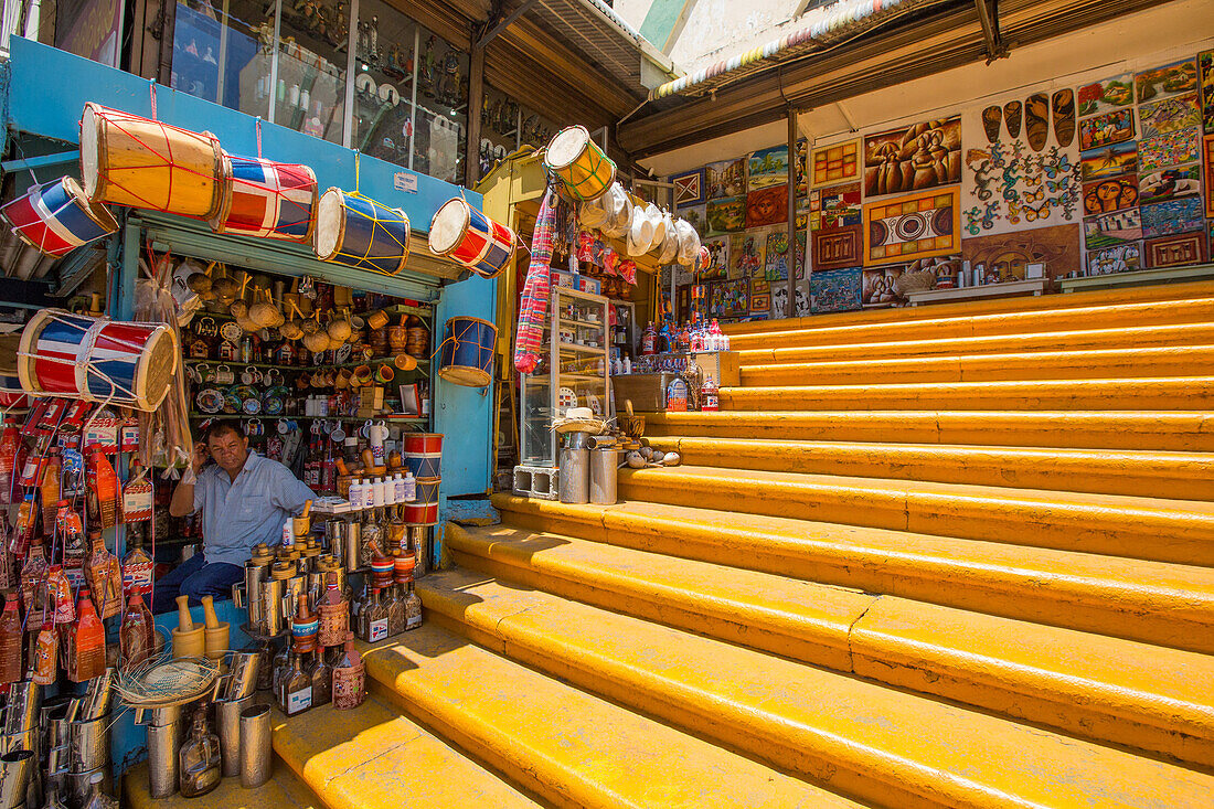 Die berühmte gelbe Treppe, die zum Mercado Modelo in Santo Domingo, Dominikanische Republik, hinaufführt. Ein Ladenbesitzer verkauft Trommeln