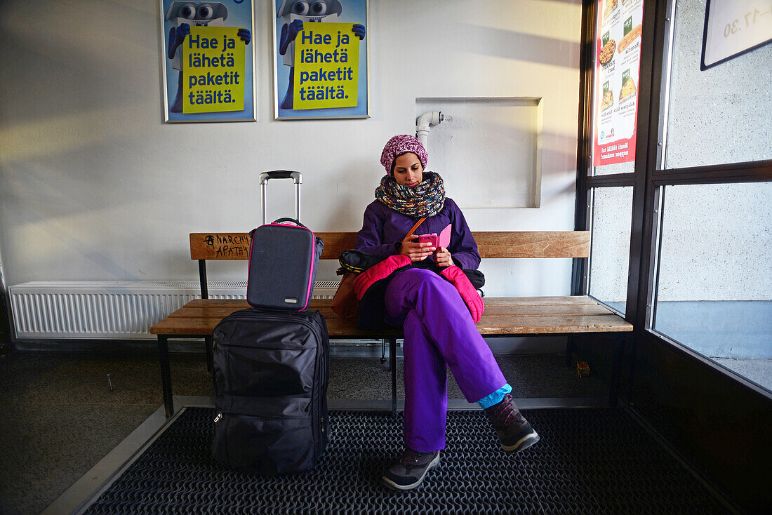 Junge Frau benutzt ihr Handy, während sie auf den Bus im Bahnhof von Kemi, Lappland, wartet