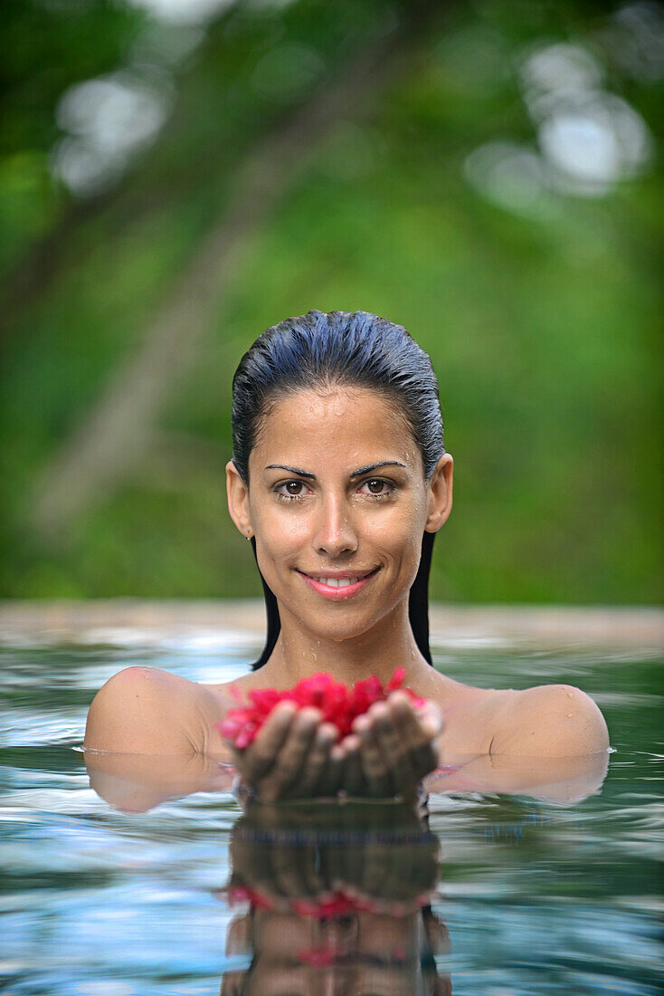 Junge attraktive Frau mit roten Blumen in einem Infinity-Swimmingpool. Das Holländische Haus, Galle, Sri Lanka