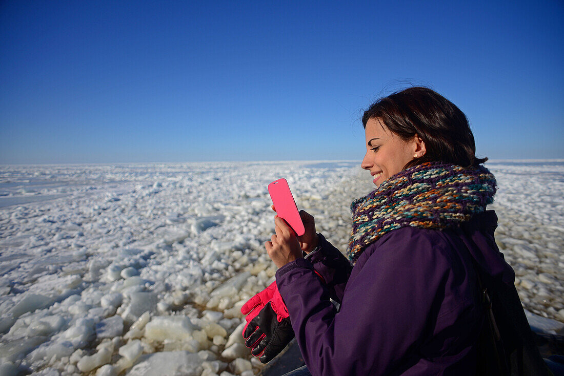 Junge Frau benutzt ein Mobiltelefon während einer Kreuzfahrt mit dem Sampo Icebreaker, einem echten finnischen Eisbrecher, der zu einer Touristenattraktion in Kemi, Lappland, umgebaut wurde