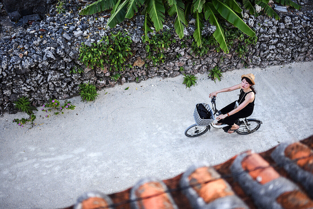 Frau fährt Fahrrad auf der Insel Taketomi, Präfektur Okinawa, Japan