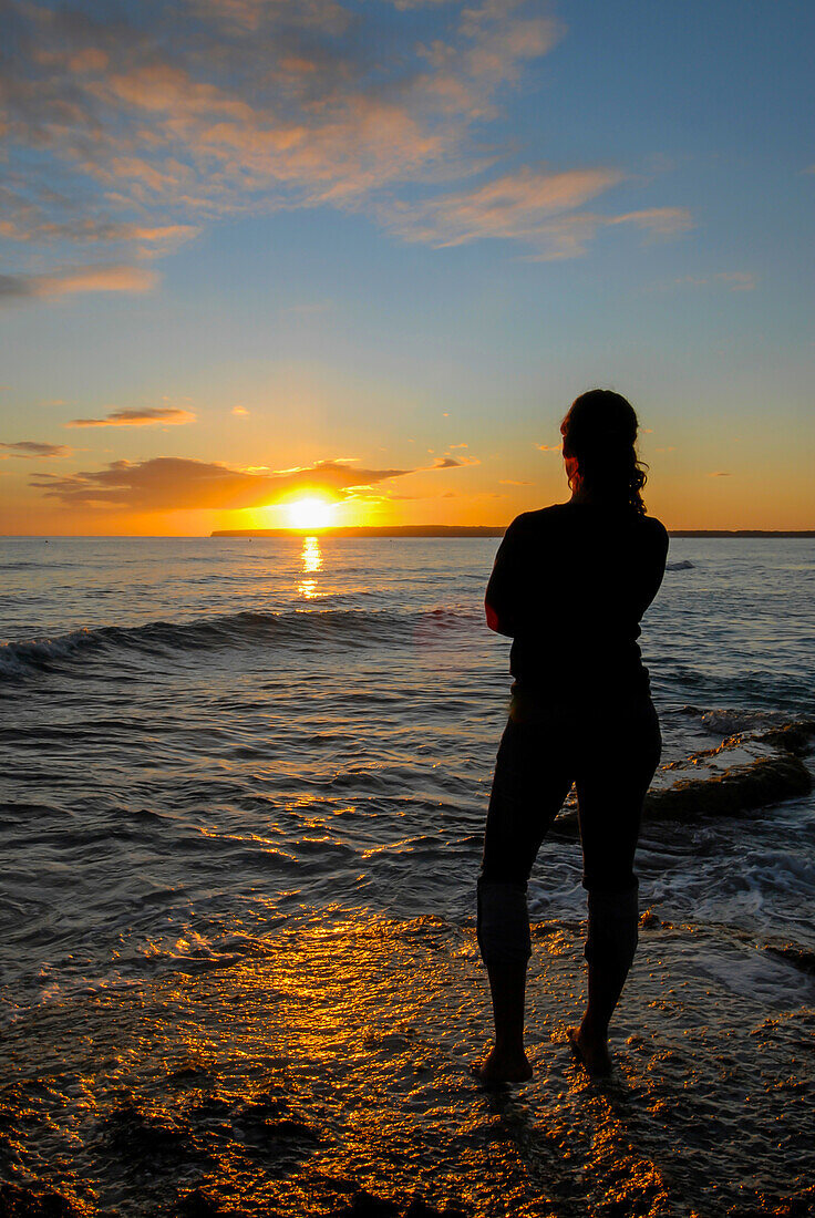 Silhouette of young woman enjoying a beautiful sunset at Migjorn beach, Formentera, Spain