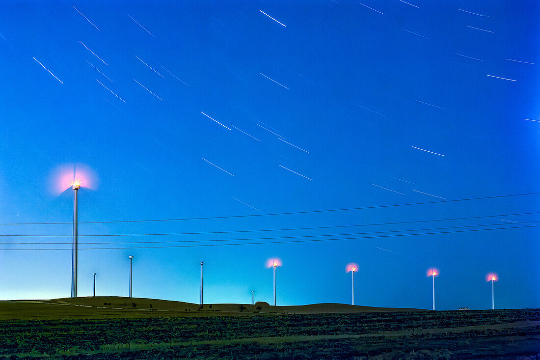 Sternennacht über spanischen Windrädern - Eine faszinierende Langzeitbelichtung, die die ruhige Schönheit von Windrädern vor dem Hintergrund von Sternenspuren am klaren Nachthimmel Spaniens einfängt