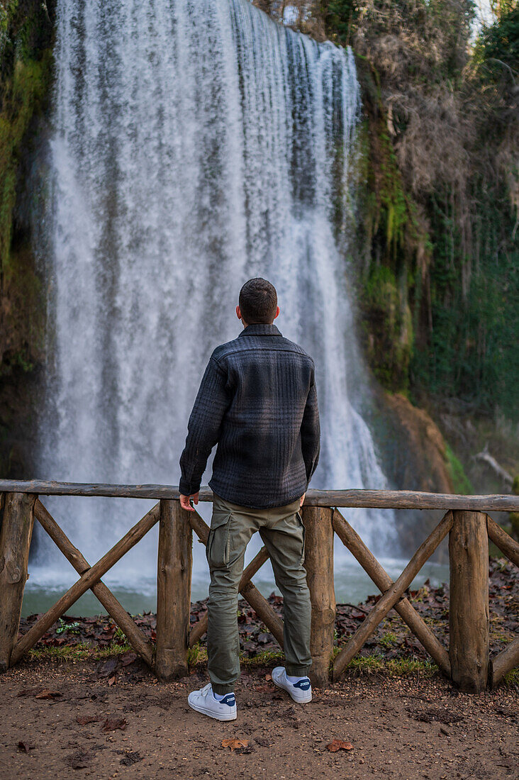 Junger Mann betrachtet einen Wasserfall im Naturpark Monasterio de Piedra, der sich um das Monasterio de Piedra (Steinkloster) in Nuevalos, Zaragoza, Spanien, befindet