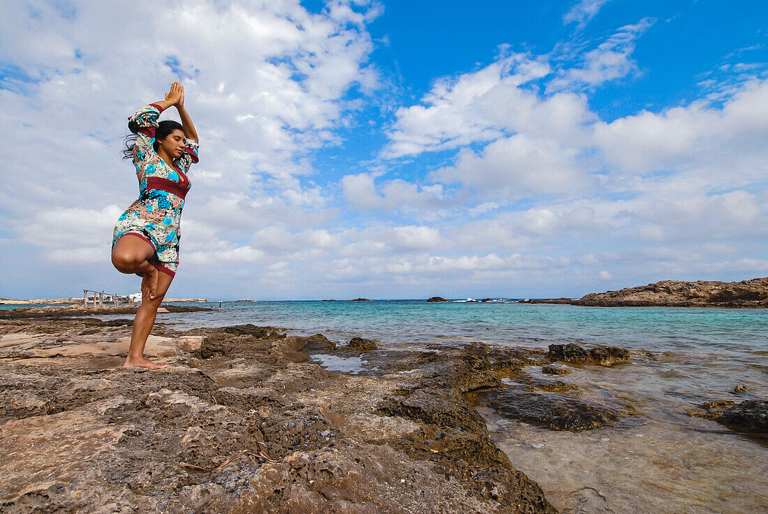 Porträt einer jungen, attraktiven brünetten Frau, die die Yoga-Baumhaltung oder Vrksasana an der Mittelmeerküste auf den Balearen, Spanien, übt