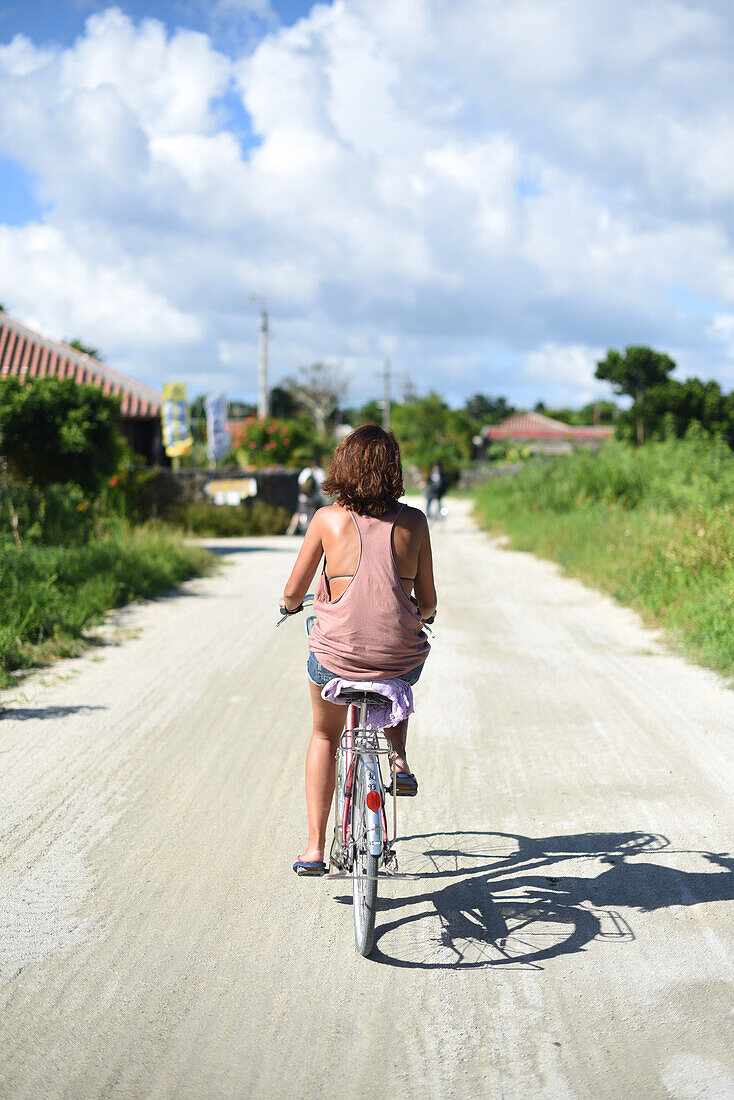 Junge Frau fährt Fahrrad auf der Insel Taketomi, Präfektur Okinawa, Japan