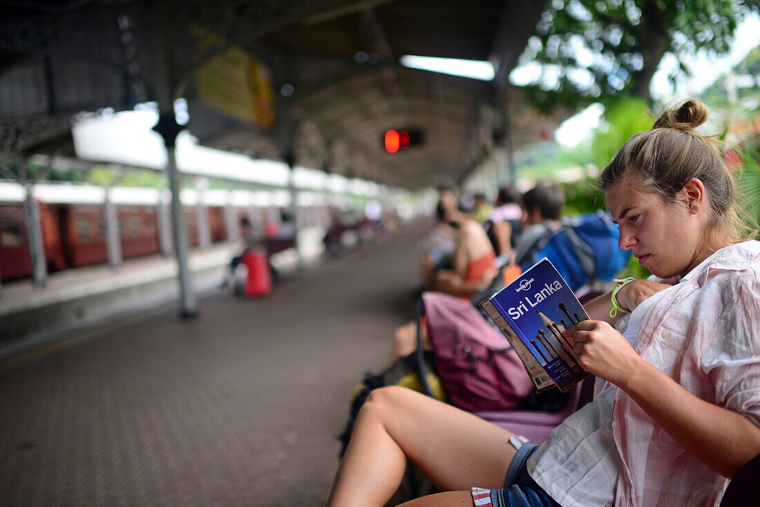 Junge Frau liest im Bahnhof von Kandy, Sri Lanka, einen Lonely Planet-Reiseführer