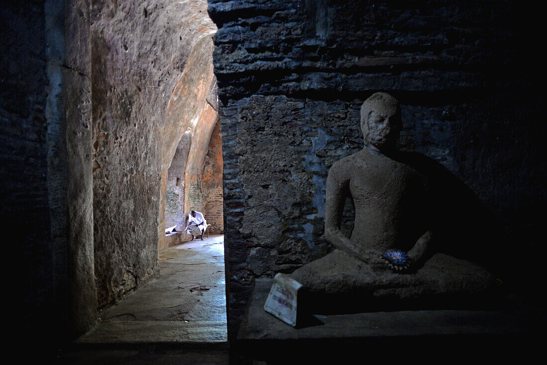 Man reading and Buddha statue Inside Thuparama at The Ancient City of Polonnaruwa, Sri Lanka