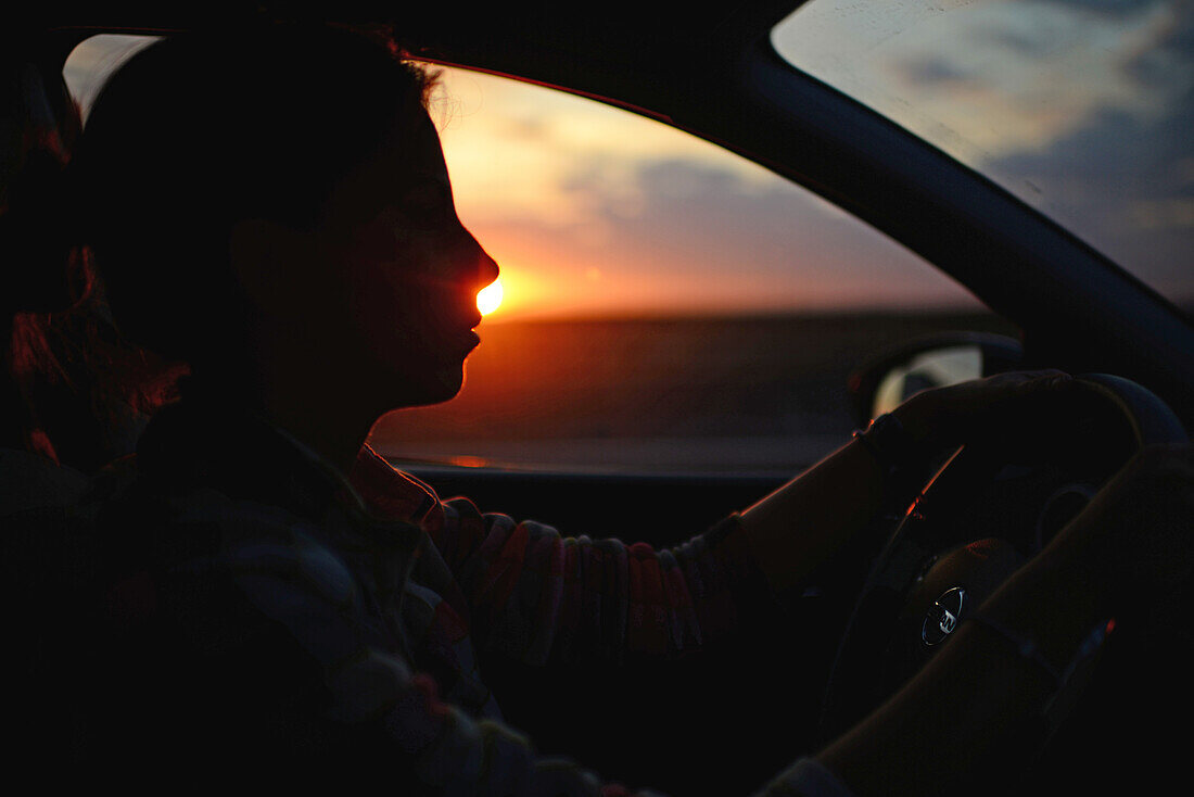 Junge Frau fährt Auto bei Sonnenuntergang
