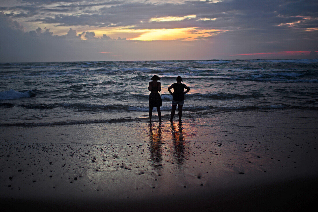 Zwei Frauen entspannen sich bei Sonnenuntergang am Strand von Hikkaduwa, Sri Lanka