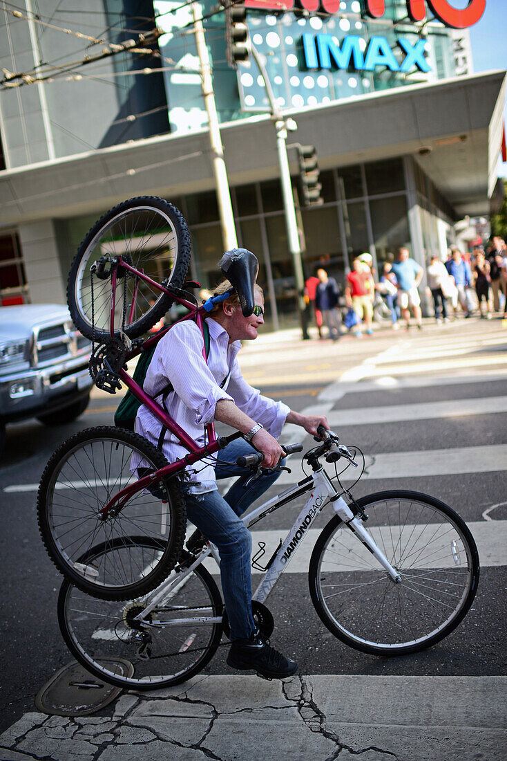 Bicycle rider carrying another bike on shoulder.