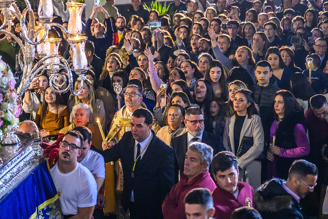 Eine faszinierte Menge versammelt sich im Schein der Nacht und betrachtet den geschmückten Wagen Unserer Lieben Frau vom Rosenkranz während einer feierlichen katholischen Prozession in Carrion de los Cespedes, Sevilla, Spanien