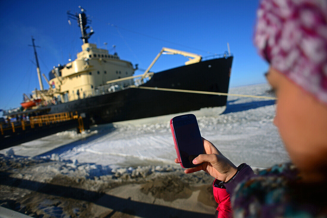 Young woman uses mobile phone to take photo of Sampo Icebreaker cruise, an authentic Finnish icebreaker turned into touristic attraction in Kemi, Lapla