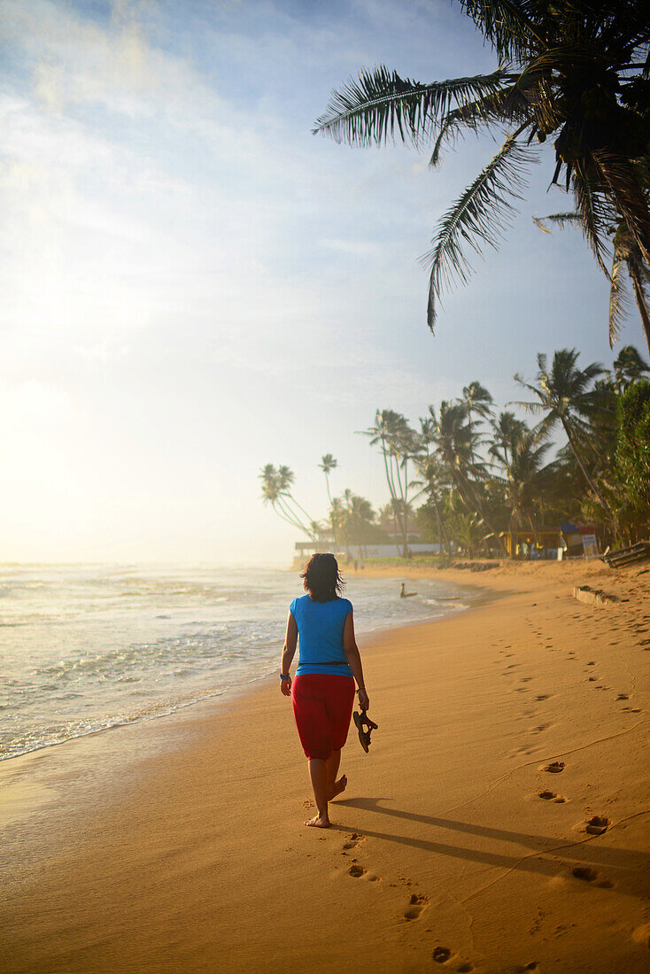 Junge Frau beim Spaziergang am Strand von Hikkaduwa bei Sonnenuntergang, Sri Lanka