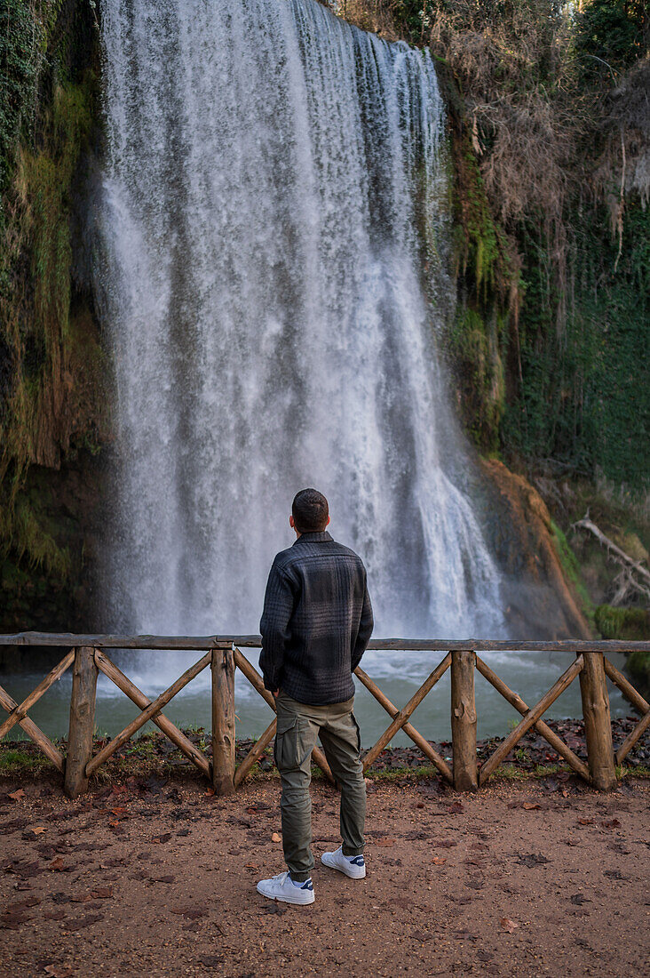 Junger Mann betrachtet einen Wasserfall im Naturpark Monasterio de Piedra, der sich um das Monasterio de Piedra (Steinkloster) in Nuevalos, Zaragoza, Spanien, befindet