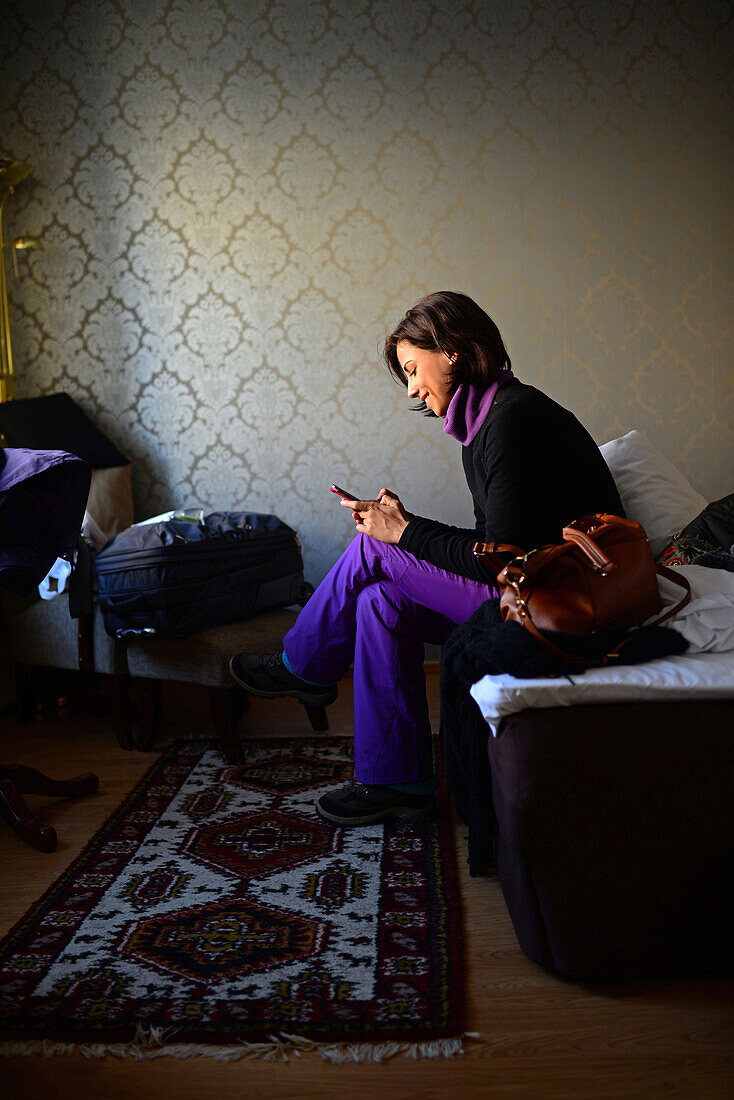 Junge Frau benutzt ein Mobiltelefon in einem Hotelzimmer, Kemi, Lappland