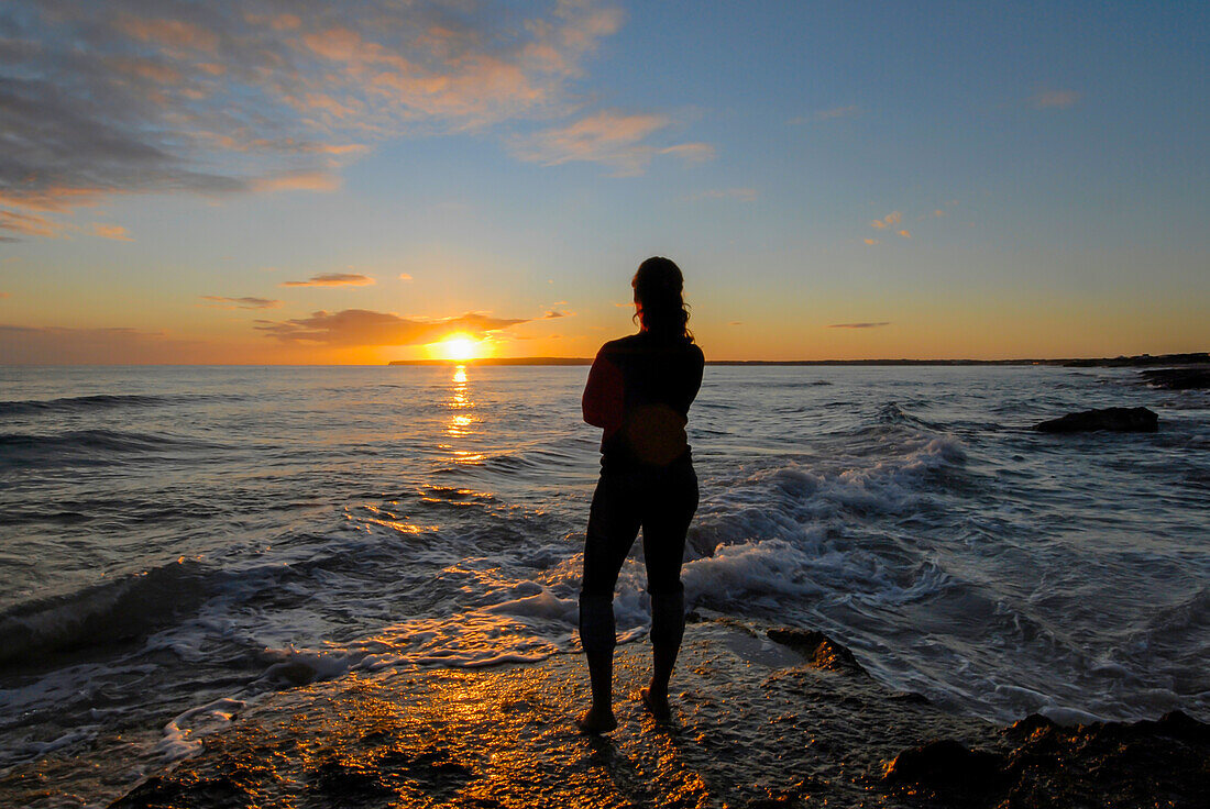 Silhouette einer jungen Frau, die einen wunderschönen Sonnenuntergang am Strand von Migjorn, Formentera, Spanien, genießt